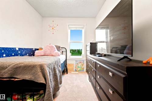 Bright room featuring a window with exterior views, light-toned carpeting, and a dark wood-finish dresser with silver hardware - 64 655 Watt Boulevard, Edmonton, AB 