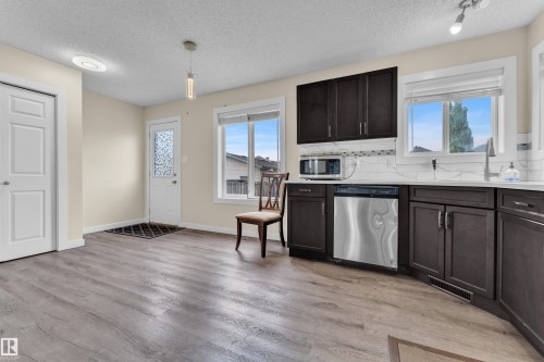 Open-concept kitchen and dining area featuring wood-finish flooring, dark wood cabinetry with stainless steel hardware, white subway tile backsplash, and a stainless steel dishwasher - 2362 29A Avenue, Edmonton, AB 