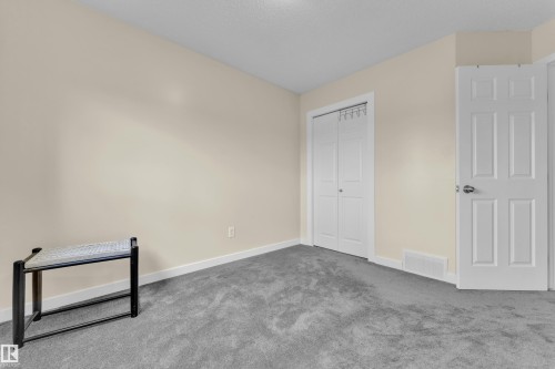 Room featuring light neutral wall paint, gray carpet flooring, white trim, a bi-fold closet door, and a paneled entry door - 2362 29A Avenue, Edmonton, AB 