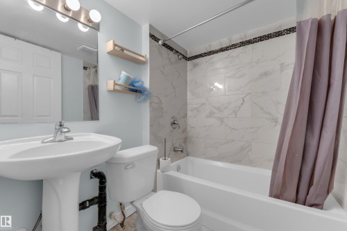 Bathroom featuring a white pedestal sink, white toilet, and a bathtub with a tiled surround - 2362 29A Avenue, Edmonton, AB 