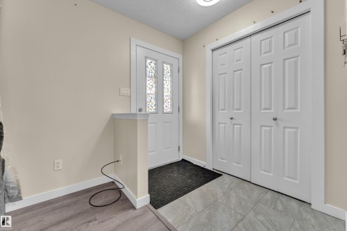 Entryway featuring a white door with decorative glass inserts, bi-fold closet doors, and mixed flooring with wood-finish planks and grey tile - 2362 29A Avenue, Edmonton, AB 