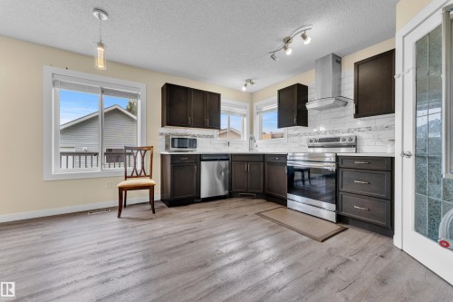 Kitchen featuring wood-finish flooring, dark cabinetry, stainless steel appliances, and light-toned countertops - 2362 29A Avenue, Edmonton, AB 