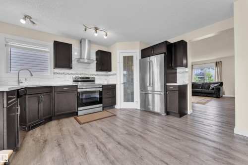 Kitchen featuring dark wood-finish cabinetry, white countertops, a subway tile backsplash, and stainless steel appliances including a refrigerator, range, and range hood - 2362 29A Avenue, Edmonton, AB 