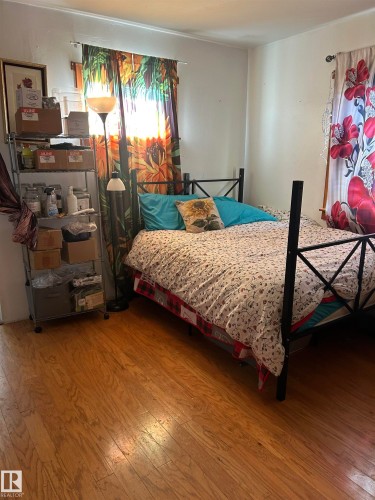 Bedroom featuring a black metal bed frame, wood-finish flooring, and ample natural light from dual windows dressed with decorative curtain panels - 5023 50 Street, Vilna, AB - Indoor Photo Showing Bedroom