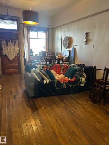 Hardwood flooring throughout, featuring paneled walls, a single window with blinds, and a drum-style pendant light fixture - 5023 50 Street, Vilna, AB - Indoor