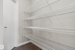 Spacious storage area featuring multiple tiers of white wire shelving, wood-finish flooring, and a contemporary paneled interior door - 