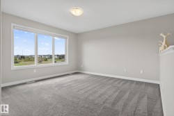 Spacious room featuring a large triple-pane window, neutral wall paint, gray patterned carpeting, white baseboards, and an overhead flush-mount light fixture - 