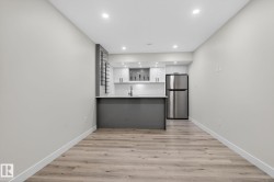 Compact kitchen featuring a stainless steel refrigerator, white cabinetry, integrated sink, and gray island with countertop seating - 