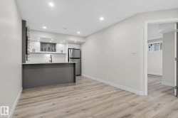 Modern kitchen space featuring a grey island with a white countertop, stainless steel refrigerator, white cabinetry, and recessed lighting - 