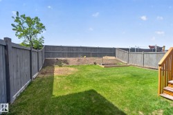 Spacious, fenced backyard featuring a manicured lawn, a raised garden bed, and a partially cultivated area - 