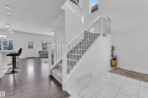 Foyer with large format marble-look tile flooring and a carpeted staircase featuring white risers and railings with metal spindles - 2630 16A Avenue, Edmonton, AB 