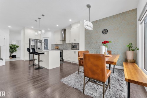Open-concept kitchen and dining area featuring dark wood-finish flooring, white cabinetry, stainless steel appliances, and a central island with pendant lighting - 2630 16A Avenue, Edmonton, AB 