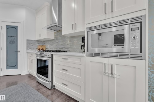 Contemporary kitchen featuring white cabinetry, stainless steel appliances, a tile backsplash, light-toned countertops, and dark wood-finish flooring - 2630 16A Avenue, Edmonton, AB 