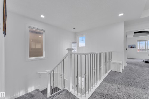 Staircase with contemporary metal balusters and white newel posts, featuring grey carpeted treads - 2630 16A Avenue, Edmonton, AB 