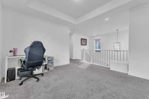Expansive open loft area featuring plush gray carpeting, white walls, a recessed tray ceiling, and a modern rectangular pendant light fixture - 2630 16A Avenue, Edmonton, AB 