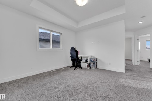 Spacious room featuring neutral carpeting, a large window with white trim, and a tray ceiling - 2630 16A Avenue, Edmonton, AB 