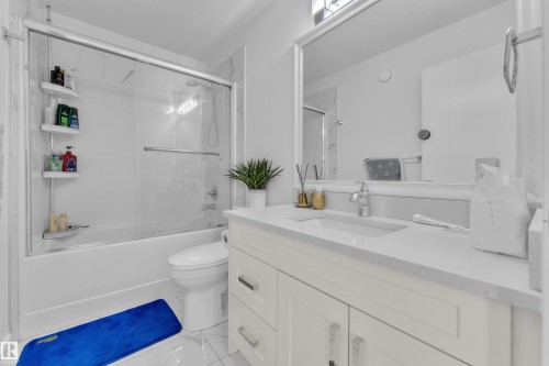 Bathroom featuring a shower/tub combination with sliding glass doors, a single vanity with a white countertop and integrated sink, a large wall-mounted mirror, and tile flooring - 2630 16A Avenue, Edmonton, AB 