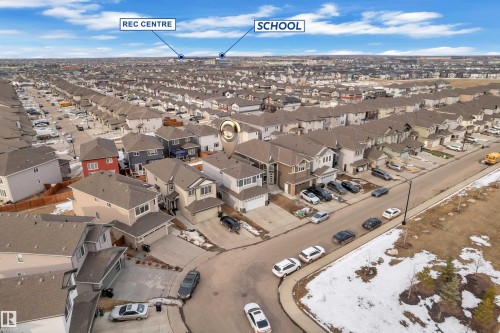 Aerial view of a residential community featuring numerous detached homes with attached garages, paved streets, and a school and recreation center in the distance - 2630 16A Avenue, Edmonton, AB 