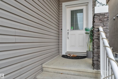 Entryway featuring a white paneled door with glass inserts, concrete steps, and a decorative stacked stone pillar - 2630 16A Avenue, Edmonton, AB 
