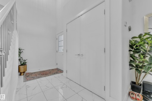 Foyer featuring white marble-effect tile flooring, a staircase with metal balusters, and a paneled entry door with sidelight - 2630 16A Avenue, Edmonton, AB 