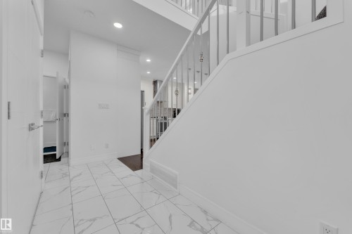 Entryway featuring white tile flooring with gray veining, white walls, and a staircase with white balusters - 2630 16A Avenue, Edmonton, AB 