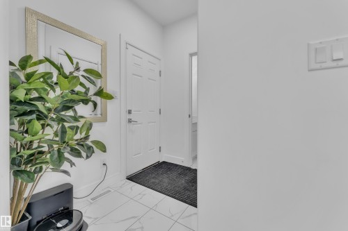 Entryway featuring white panel door, light tile flooring with subtle veining, and a wall-mounted rectangular mirror with a textured frame - 2630 16A Avenue, Edmonton, AB 