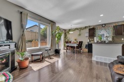 Open-concept living area featuring wood-finish flooring throughout, a large window with direct yard access, and a dining area with a contemporary chandelier - 