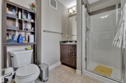 Bathroom featuring a walk-in shower with a glass enclosure, a dark wood-finish vanity with a stone countertop, and a white toilet with an integrated shelving unit - 