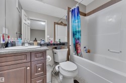 Bathroom featuring a white bathtub and shower surround, a white toilet, and a wood-finish vanity with a countertop sink - 