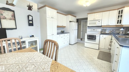 Kitchen featuring white cabinetry with light wood-finish trim, a full suite of white appliances, and a patterned floor - 13307 Delwood Road, Edmonton, AB 
