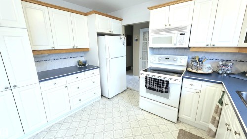 Kitchen featuring white cabinetry with brushed nickel hardware, laminate countertops, white tile backsplash with decorative accent, and patterned resilient flooring - 13307 Delwood Road, Edmonton, AB 