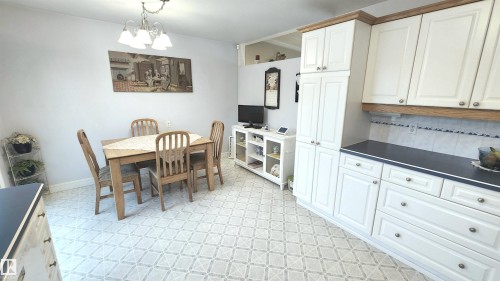 Kitchen and dining area featuring white cabinetry with wood-finish trim, dark countertops, and a tile backsplash - 13307 Delwood Road, Edmonton, AB 