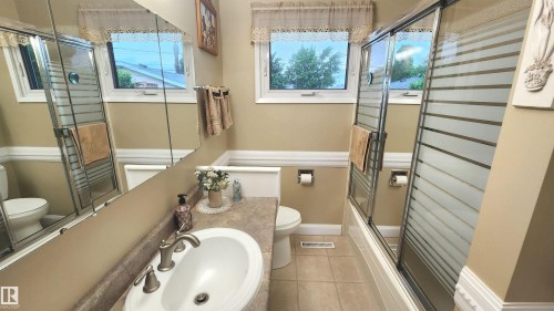 Bathroom featuring a single vanity with a white basin sink, brushed nickel faucet, and a patterned countertop - 13307 Delwood Road, Edmonton, AB 