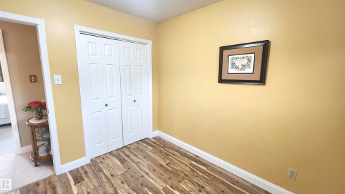 Room featuring wood-finish flooring, white baseboards, and a bi-fold closet with panel doors - 13307 Delwood Road, Edmonton, AB 