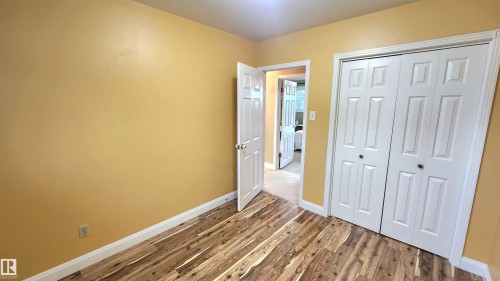 Room featuring wood-finish flooring, warm-toned walls, white baseboards, and a built-in closet with bi-fold doors - 13307 Delwood Road, Edmonton, AB 