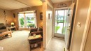 Entryway with a solid white door and decorative glass insert, opening to a living area featuring a large bay window, textured carpeting, and exposed ceiling beams - 13307 Delwood Road, Edmonton, AB 