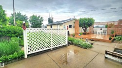 Expansive backyard featuring a multi-level wood deck, white lattice privacy screen, concrete patio, and garden beds with mature plantings - 