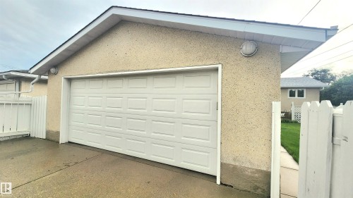 Detached garage featuring a paneled overhead door, stucco exterior, and white picket fence - 13307 Delwood Road, Edmonton, AB 