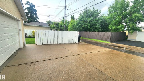 Expansive concrete driveway providing access to the attached garage, bordered by a white picket fence and a tall privacy fence - 13307 Delwood Road, Edmonton, AB 