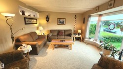 Living room featuring a large bay window, light-toned patterned carpeting, a built-in display nook, crown molding, and neutral wall tones - 