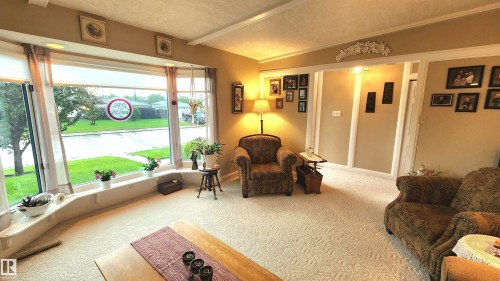 Living area featuring a wide bay window with a built-in sill, light-toned patterned carpeting, and painted interior walls with decorative trim - 13307 Delwood Road, Edmonton, AB 