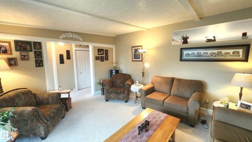 Spacious living room featuring light-toned walls, a wide archway with white trim, and white ceiling beams - 13307 Delwood Road, Edmonton, AB 