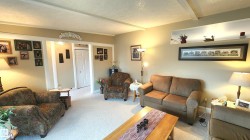 Spacious living room featuring light-toned walls, a wide archway with white trim, and white ceiling beams - 