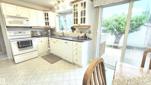White cabinetry kitchen featuring a built-in microwave, tile backsplash, and dark countertops, with patterned flooring - 13307 Delwood Road, Edmonton, AB 