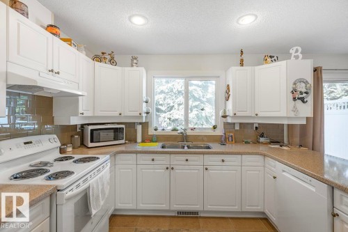 Bright kitchen featuring white cabinetry, light-toned countertops, a tile backsplash, recessed lighting, and a double basin sink - 44 9630 176 Street, Edmonton, AB 