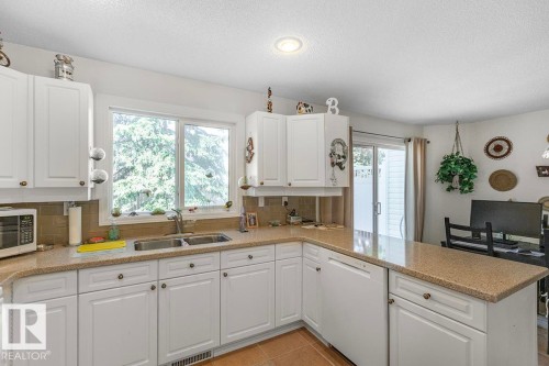 Kitchen featuring white cabinetry, a double basin stainless steel sink, light-colored countertops, and a full-size window - 44 9630 176 Street, Edmonton, AB 