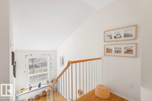 Staircase featuring wood-finish flooring, white balusters, and a natural wood handrail - 44 9630 176 Street, Edmonton, AB 