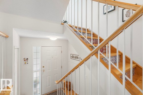 Entryway featuring a white paneled door with sidelight, overhead lighting, and a staircase with wood treads, patterned risers, and a wood handrail - 44 9630 176 Street, Edmonton, AB 