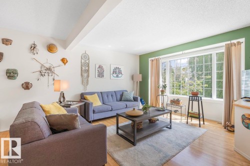 Spacious living area featuring wood-finish flooring, a large multi-pane window, and a painted accent wall - 44 9630 176 Street, Edmonton, AB 