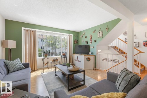 Living room featuring light wood-finish flooring, a large multi-pane window, and a prominent staircase with white balusters and wood handrails - 44 9630 176 Street, Edmonton, AB 